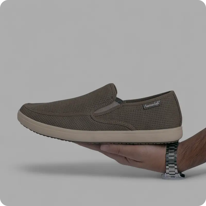 Brown perforated slip-on shoe held in one hand